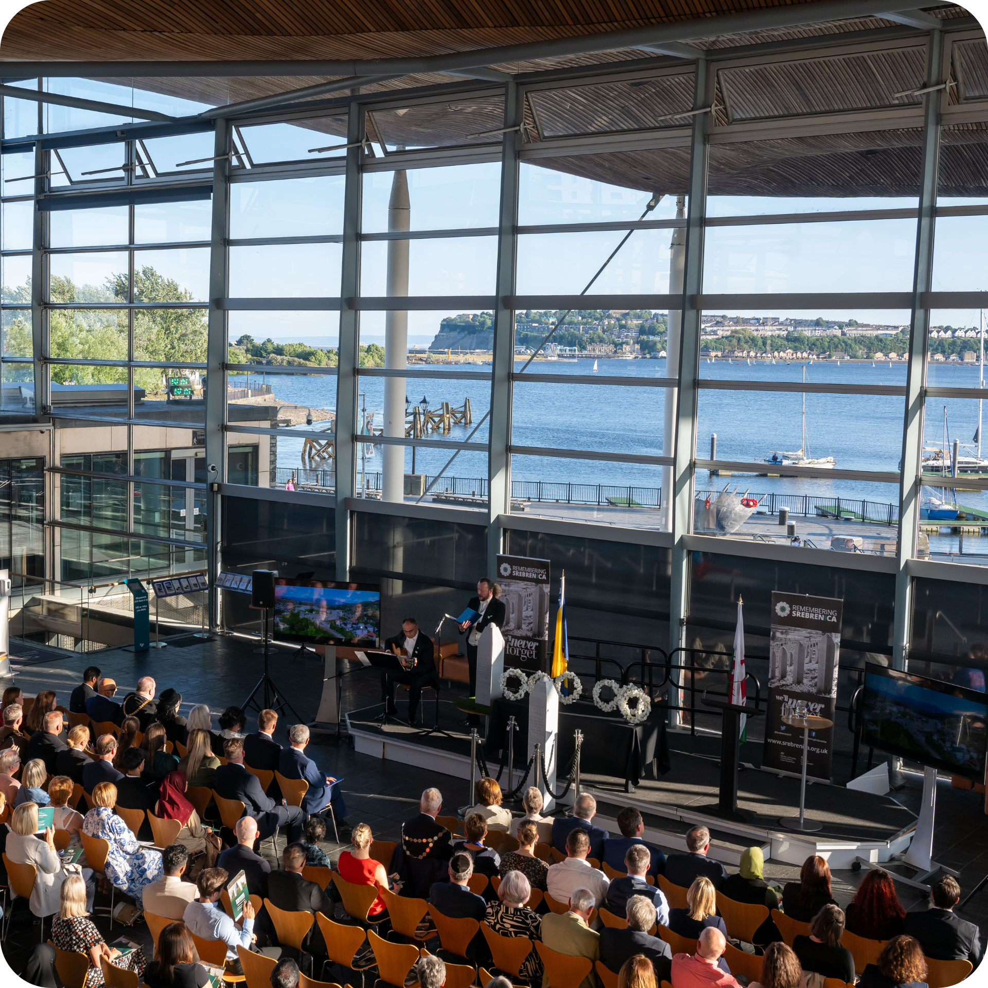 Llun yn dangos ymwelwyr yn eistedd mewn digwyddiad yn y Senedd, yn wynebu’r ffenestr flaen tra bod siaradwr ar y llwyfan.