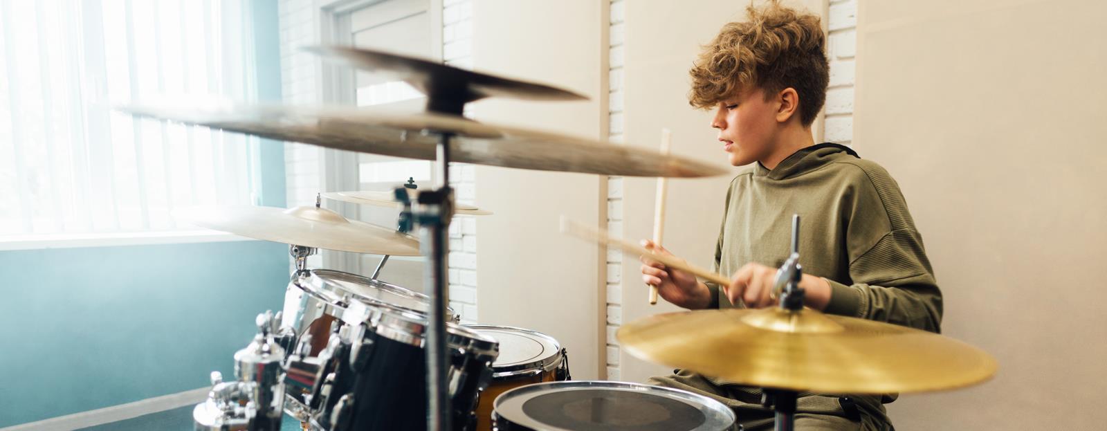 A teenage boy practicing on a drum kit. 